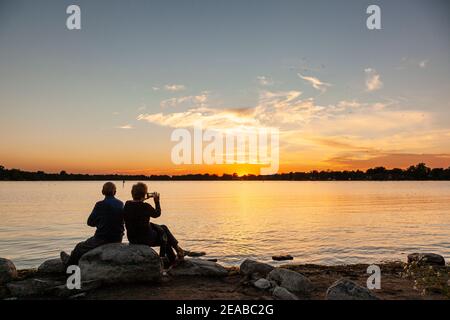 Un couple de personnes âgées s'est défait sur un magnifique coucher de soleil sur un lac. Banque D'Images