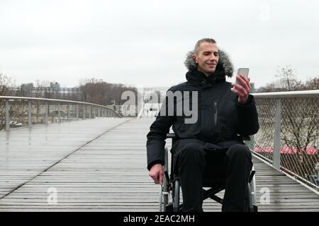 Concept de personne handicapée. Homme en fauteuil roulant à l'extérieur de la rue. Les utilisateurs de la technologie avec un smartphone. Banque D'Images