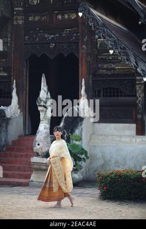 Portrait de la femme thaïlandaise avec la traditionnelle robe thaïlandaise marchant avec arrière-plan du temple Banque D'Images