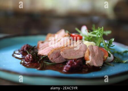 Confit de canard avec salade , pomme au four et sauce aux framboises servi sur table en bois Banque D'Images