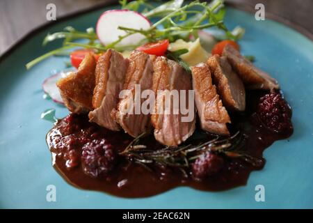 Confit de canard avec salade , pomme au four et sauce aux framboises servi sur table en bois Banque D'Images