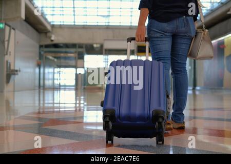 Une vue de dos, moitié inférieure du corps d'une femme en Jean, marchant dans un terminal d'aéroport, tirant sa valise bleue le long dans le dos, se préparer à b Banque D'Images