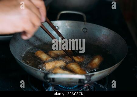 Faire frire les rouleaux à ressort dans une poêle à l'aide de baguettes. Banque D'Images