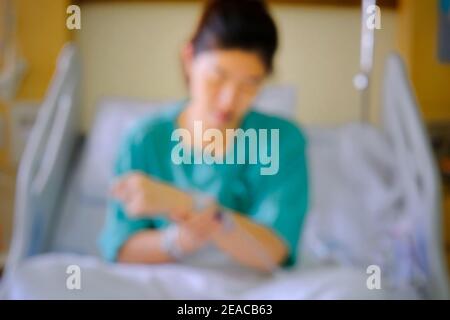 Une image hors du foyer d'une femme asiatique traitée pour sa maladie dans une chambre d'hôpital, assise sur un lit avec un uniforme vert et une solution saline Banque D'Images