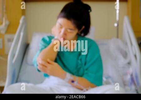 Une image hors du foyer d'une femme asiatique traitée pour sa maladie dans une chambre d'hôpital, assise sur un lit avec un uniforme vert et une solution saline Banque D'Images