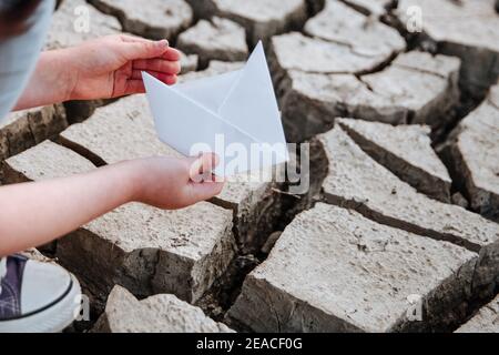 La fille abaisse le bateau en papier sur le sol sec et fissuré. Crise de l'eau et changement climatique concept. Réchauffement de la planète Banque D'Images