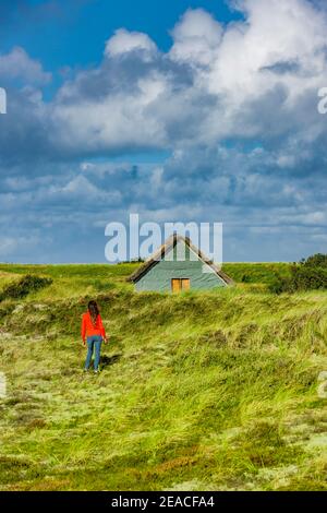 Femme avec un chandail rouge dans les dunes à l'avant d'une maison de toit de chaume Banque D'Images