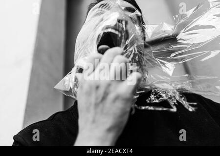 Un homme caucasien avec suffocation et colère portant un plastique sac sur sa tête et crier Banque D'Images