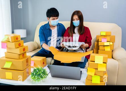 couple en ligne entrepreneur emballant une boîte à colis pour la livraison au bureau à domicile, les personnes portant un masque facial pour protéger le coronavirus (covid-19) pandémie Banque D'Images