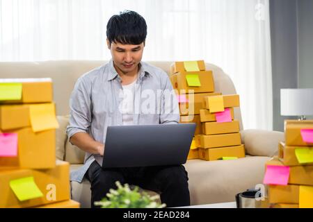 Homme entrepreneur travaillant avec un ordinateur portable et vérifiant pour préparer des boîtes à colis à livrer au client à domicile (PME) Banque D'Images