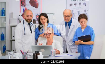 Équipe médicale discutant du diagnostic des problèmes de traitement des patients sur le lieu de travail à l'aide d'un ordinateur portable. Groupe de médecins, travail d'équipe personnes ayant la santé conférence de brainstorming dans la salle de réunion de l'hôpital. Banque D'Images