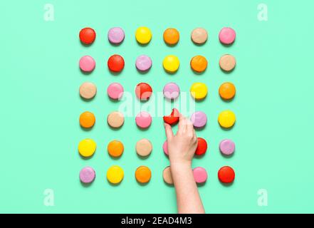 Macarons biscuits alignés dans une forme carrée, isolés sur un fond vert. Femme attrapant un cookie d'amande. Manger un macaron français coloré. Banque D'Images