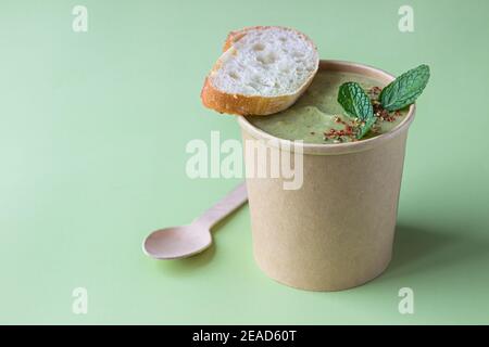 Soupe à la crème de brocoli fraîche servie avec du pain frais, de la menthe et des épices dans un récipient artisanal sur fond vert. Soupe à emporter, alimentation saine. Sélection Banque D'Images