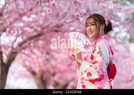 femme à yukata (robe kimono) tenant le ventilateur pliable et regardant la fleur de sakura ou de cerisier floraison dans le jardin Banque D'Images