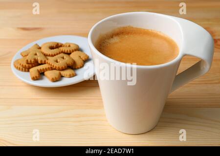 Bouchez une tasse de café mousseux chaud avec une assiette de biscuits sur table en bois Banque D'Images