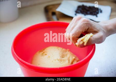 Femme qui colle (pétrit) la pâte à biscuits avec ses mains dans un bol rouge. La femme adulte se fait cuire des biscuits délicieux et croquants en cas de pandémie Banque D'Images