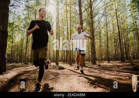 Père caucasien et fils adolescents frères s'exerçant dans une forêt luxuriante courir dans les bois Banque D'Images