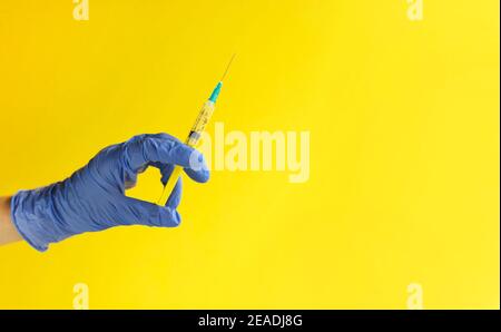 Gros plan de la main du médecin dans un gant bleu tenant une seringue en plastique sur fond jaune. Injection médicale. Covid-19 vaccination, soins de santé, traitement con Banque D'Images