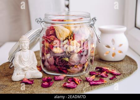 Utiliser des pétales de rose secs pour faire de la roseraie, ce qui est idéal pour les senteurs à la maison. Pot Mason rempli de pétales de rose secs et de puds avec Bouddha méditant. Banque D'Images