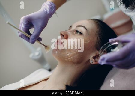 Esthéticienne appliquant avec le gel de contact de brosse sur le visage de la femme pour les procédures de matériel dans le spa de beauté. Banque D'Images