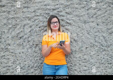 Jeune femme du millénaire portant des lunettes regardant l'appareil photo et souriant tout en tenant un téléphone mobile pour communiquer avec des amis et des collègues Banque D'Images