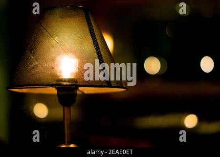 Gros plan d'une lampe avec abat-jour sombre et lumière chaude dans une pièce sombre et sombre. Une lampe à l'avant et d'autres tours flous en arrière-plan. Côté droit Banque D'Images