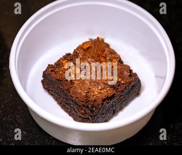 Gros plan d'un Brownie d'amande au chocolat dans une boîte à emporter blanche sur fond de granit noir. Banque D'Images