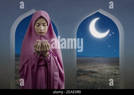 Femme musulmane asiatique sous un voile debout et mains levées et prier sur la mosquée Banque D'Images