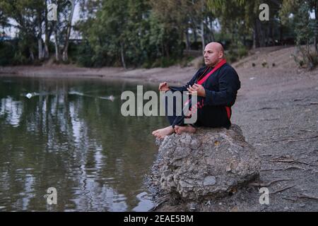 artiste martial méditant à un lac avec noir et rouge kimono Banque D'Images