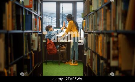 Bibliothèque de l'université: Garçon utilise un ordinateur personnel à son bureau, parle avec la femme classmate donner High cinq après la solution réussie. Étude ciblée des étudiants Banque D'Images