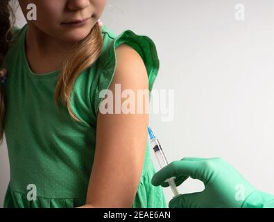 Concept de vaccination. Médecin en gants faisant la vaccination de la petite fille mignonne en robe verte en clinique Banque D'Images