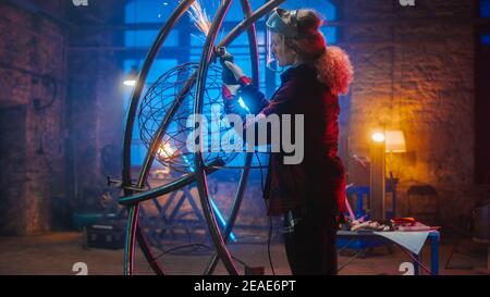 Talentueux artiste féminin Tomboy innovant utilise un meuleuse d'angle pour faire une sculpture de métal abstraite, brutale et expansive dans un atelier. Contemporain Banque D'Images