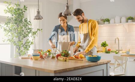 Dans la cuisine : couple parfaitement heureux préparer des aliments sains, beaucoup de légumes. L'homme jongle avec des fruits, fait rire sa petite amie. Les gens sont charmants Banque D'Images