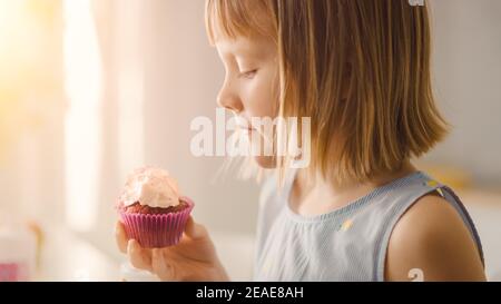 Dans la cuisine : adorable petite fille mange un gâteau crémeux avec des confettis dépoliés et saupoudrées. Mignon petit garçon affamé Bites enfant dans Muffin avec Banque D'Images