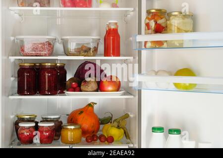 Des bocaux avec confitures maison de fruits et de baies, jus de fruits et autres produits sur une étagère dans le réfrigérateur. Les aliments sains fermentés sont au réfrigérateur. Banque D'Images