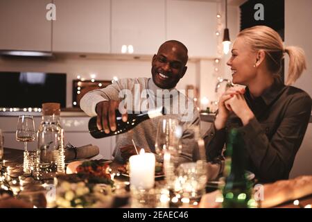 Homme versant un verre de vin à un ami pendant un dîner aux chandelles autour d'une table avec des amis Banque D'Images