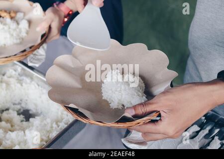 La main de la personne met le riz blanc de la casserole d'acier à assiette en papier en bois pour le déjeuner au restaurant Banque D'Images