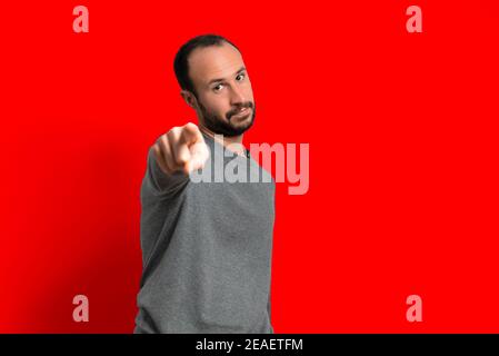 jeune homme pointant le doigt vers l'appareil photo en studio portrait sur fond rouge. attitude confiante de réussite et de confiance en soi. espace de copie Banque D'Images
