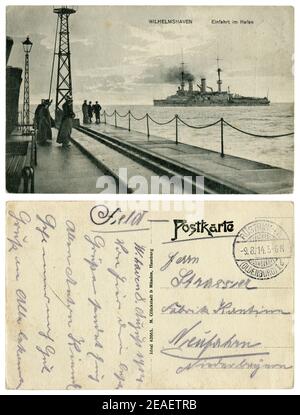 Carte postale historique allemande : jetée à l'entrée du port de Wilhelmshaven. Les femmes et les hommes regardent le navire de guerre. Guerre mondiale un 1914-1918 Banque D'Images