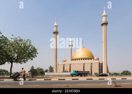 Abuja, Nigeria - 27 janvier 2021 : un homme pousse une roue à cardans le long d'une autoroute vide en face du bâtiment historique de la mosquée nationale à Abuja, au Nigeria. Banque D'Images