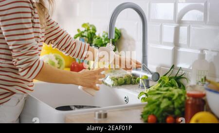 Gros plan d'une femme qui remplit une bouteille en plastique réutilisable avec de l'eau du robinet propre et filtrée. Utiliser une bouteille de sport pour l'hydratation dans une cuisine moderne Banque D'Images