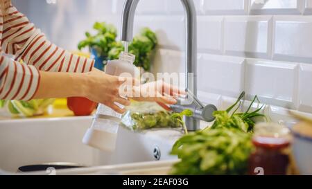 Gros plan d'une femme qui remplit une bouteille en plastique réutilisable avec de l'eau du robinet propre et filtrée. Utilisation d'une bouteille de sport pour H2O dans une cuisine moderne. Naturel Banque D'Images