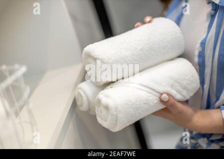 Les mains de la femme mettent ou présentent une serviette blanche enroulée propre en coton biologique. Banque D'Images