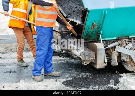 Les travailleurs utilisent des pelles pour nettoyer un finisseur d'asphalte devant les éléments de construction d'une nouvelle section de la route. Mise au point sélective. Banque D'Images