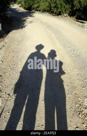 De longues ombres d'un homme et d'une femme marchant sur une route de campagne poussiéreuse et non métalée pendant un après-midi ensoleillé. Andalousie, Espagne Banque D'Images