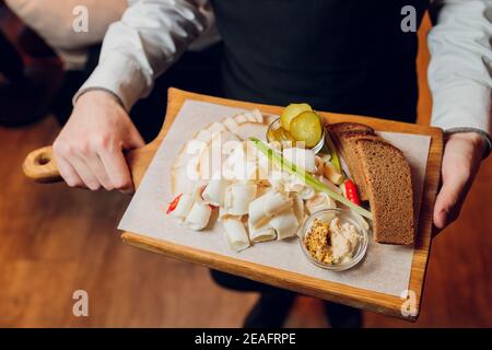 Dans un beau restaurant, un serveur apporte un plat prêt à l'emploi pour un jeune homme en costume, sur un plateau de saindoux en chêne avec de l'ail. Concept de: Ail, l Banque D'Images