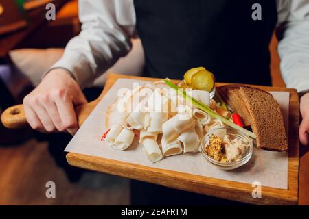 Dans un beau restaurant, un serveur apporte un plat prêt à l'emploi pour un jeune homme en costume, sur un plateau de saindoux en chêne avec de l'ail. Concept de: Ail, l Banque D'Images