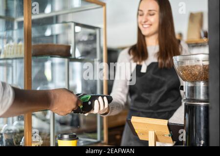 Serveuse souriante donnant un terminal de paiement de pos à un client afro-américain, une main masculine utilise une méthode sans contact pour payer la commande dans un café Banque D'Images