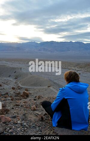 une personne assise sur une pierre dans le ciel du soir avec le soleil se brisant à travers les nuages avec une vue à La gamme panamint et le lavage de la vallée de la mort en t Banque D'Images