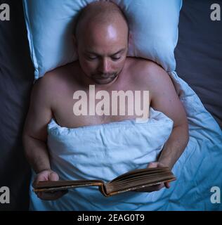 Homme lisant un livre au lit la nuit. Banque D'Images